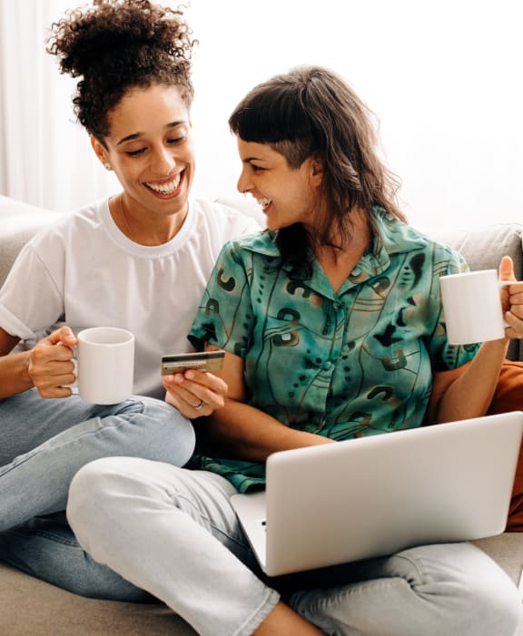 two women sitting on a couch drinking coffee while using a laptop computer at North Grove, Riverside, CA