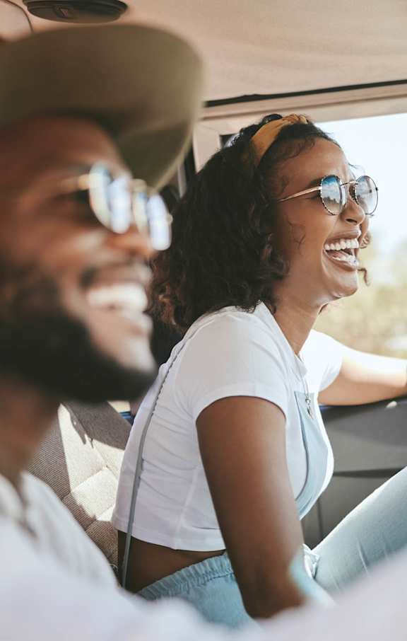 A man and a woman are sitting in a car, both wearing sunglasses and enjoying a sunny day out.