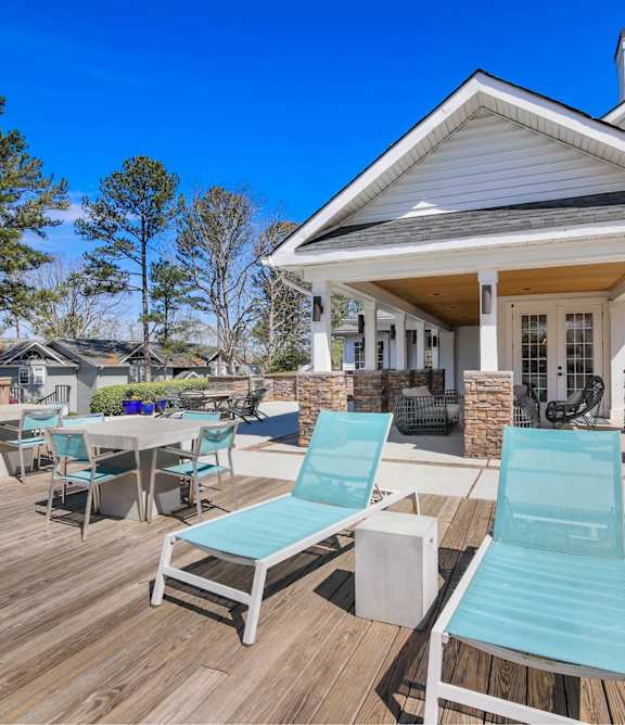 A white house with a wooden deck and blue lounge chairs.