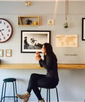 a woman sits on a stool in a cafe with a clock on the wall behind her