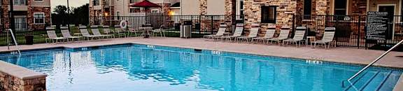 A swimming pool surrounded by a stone wall and lounge chairs.