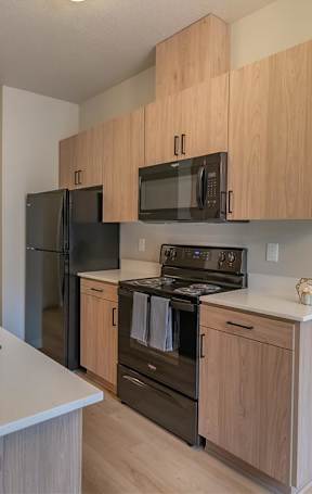 A modern kitchen with wood cabinets and black appliances at Woodburn Place Apartment Homes, Woodburn, OR, 97071