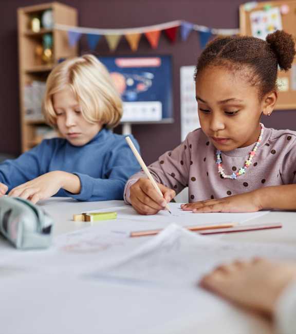Three children are sitting at a table, focused on their artwork.