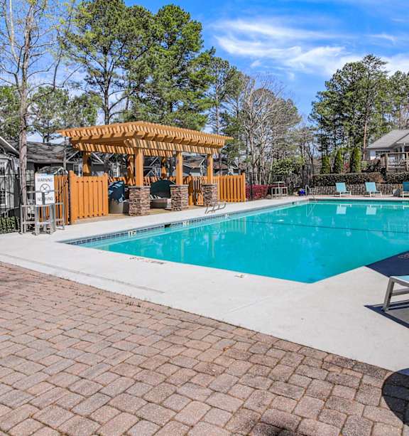 A pool area with a gazebo and lounge chairs.