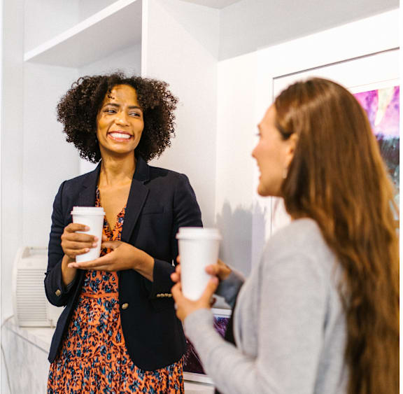Two women having a conversation while holding coffee cups.