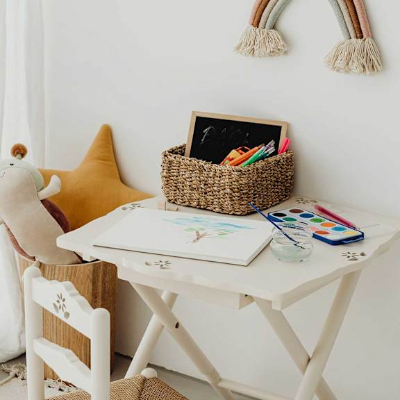 A white desk with a yellow star-shaped pillow and a white chair with a wooden design.
