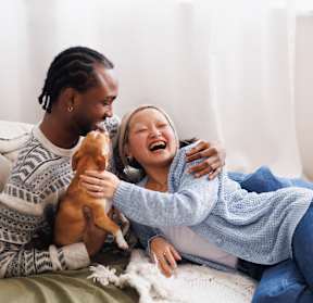 A man and a woman are sitting on a bed with a dog between them.