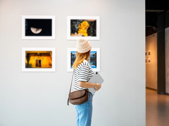 A woman in a striped shirt and hat is looking at artwork on a wall.