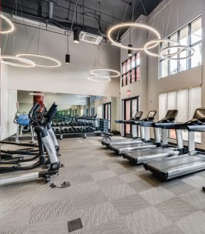 a row of treadmills and elliptical trainers in a fitness room with large windows
