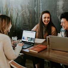Three people are sitting at a table with laptops open in front of them.