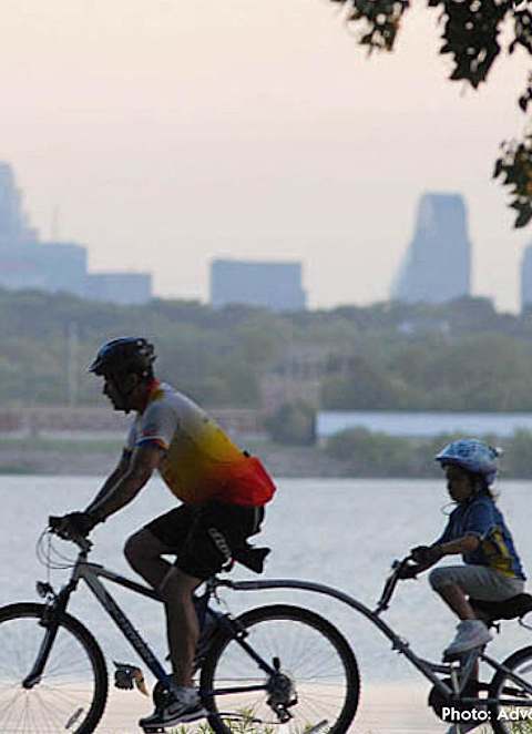 Two people riding bikes on a body of water with a city skyline in the background.