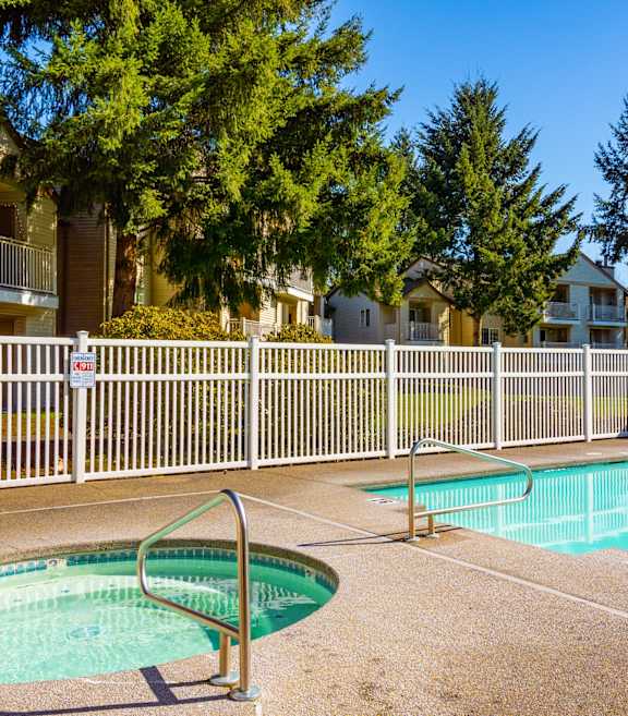 A small pool with a hot tub in the middle of a fenced in area.
