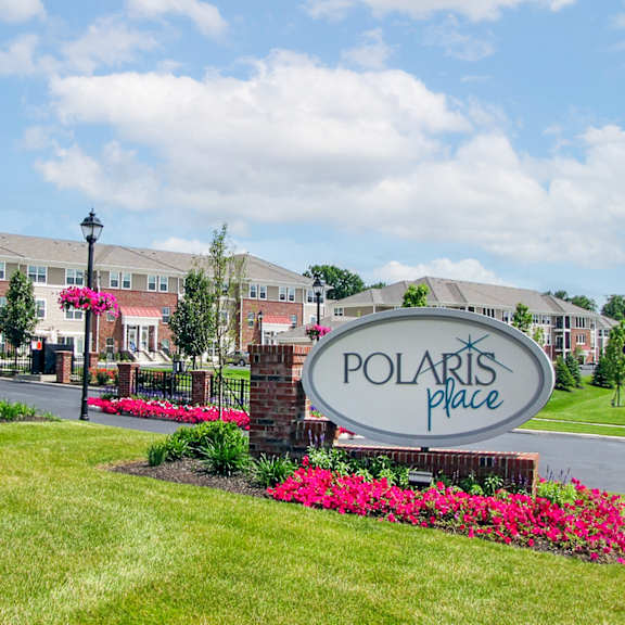 A sign for Polaris Place is in front of a building and some bushes.