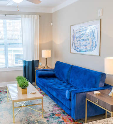 A blue couch sits in a living room with a white chair and a small table with a plant on it. at Fox Hollow Apartment Homes, High Point, NC, 27265