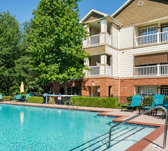 A large swimming pool surrounded by a brick border and a building in the background.