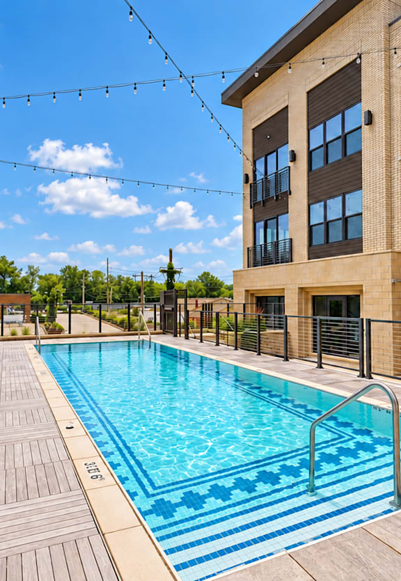 A pool surrounded by lounge chairs and apartment buildings.