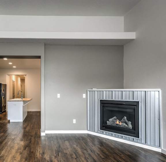 A modern living room with a fireplace and a kitchen in the background.