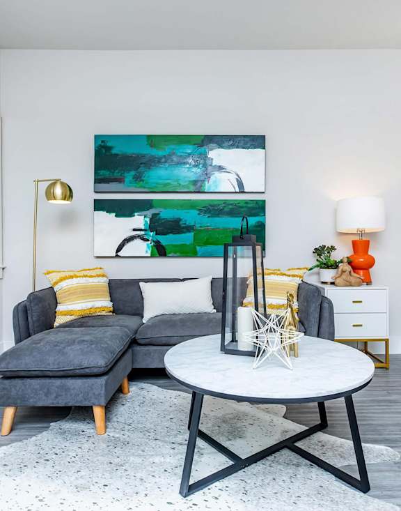 A modern living room with a grey sofa, a white coffee table, and a large abstract painting on the wall. at Sienna at Westover Hills Apartments, San Antonio, TX 78253