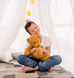 A boy is sitting inside a white tent holding a teddy bear.