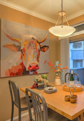 a dining area with a wooden table and chairs and a painting of a cow on the wall