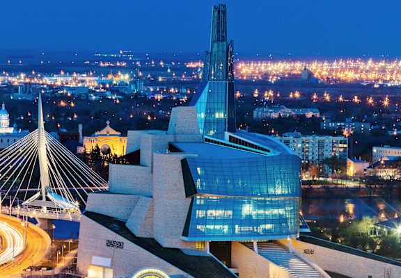 A cityscape at night with a prominent building featuring a spire and a bridge in the foreground.