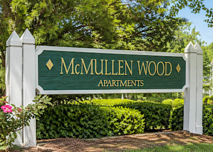 A green sign that says McMullen Wood Apartments stands in front of a building.