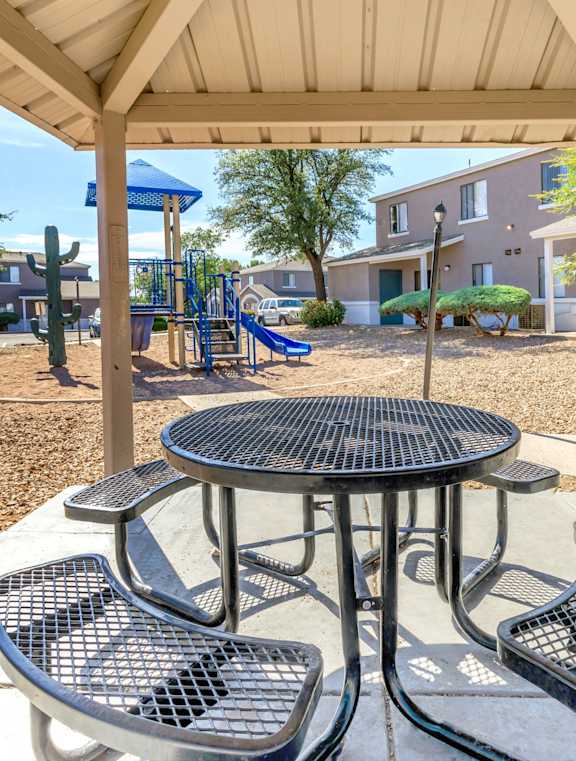 A playground with a table and chairs under a canopy.