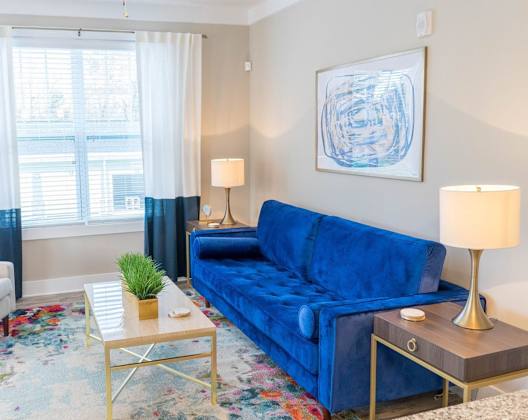 A blue couch sits in a living room with a white chair and a small table with a plant on it.