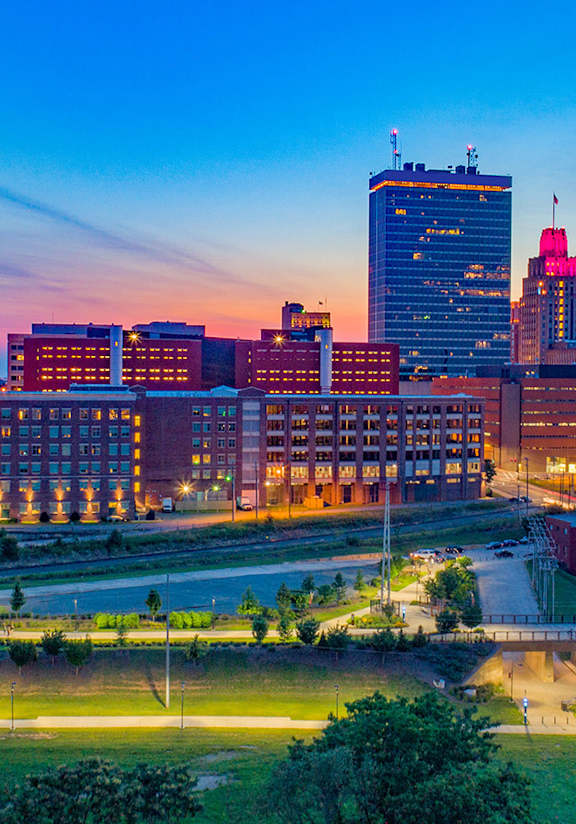 A city skyline at dusk with a prominent building featuring a large dome-like structure.