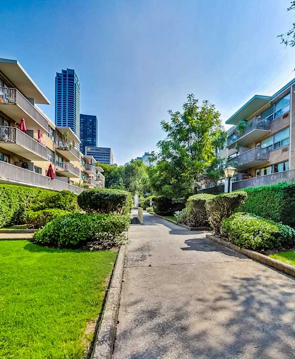 a path between two apartment buildings with green grass and trees