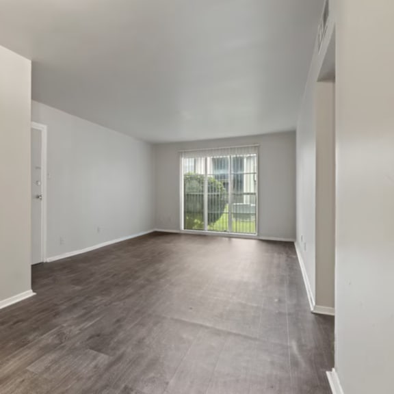 A spacious empty room with wooden flooring and white walls.