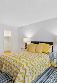 A bedroom with a bed covered in yellow and white bedding at Verandas Apartments, West Covina, CA, 91791