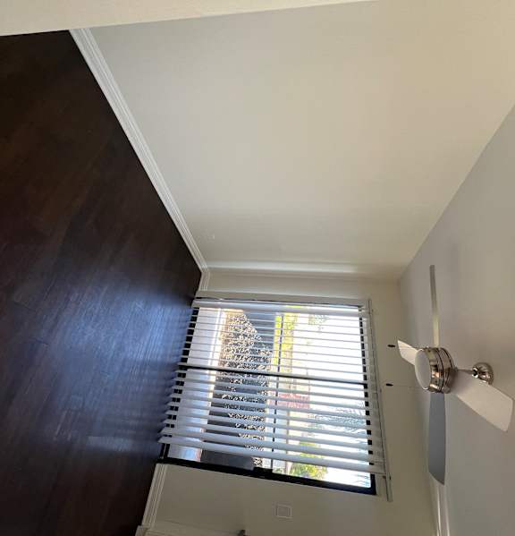 A white fan is mounted on a wall next to a window with blinds.
