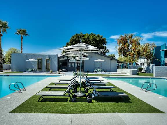 A poolside area with sun loungers and a white building in the background. at Connect on Missour Apartments, Phoenix 85015