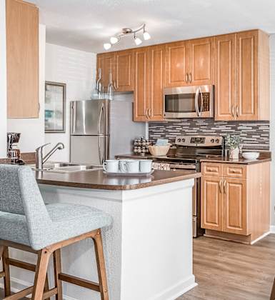 A kitchen with wooden cabinets and a white island with a chair. at Central on the Green Apartment Homes, North Carolina, 27604