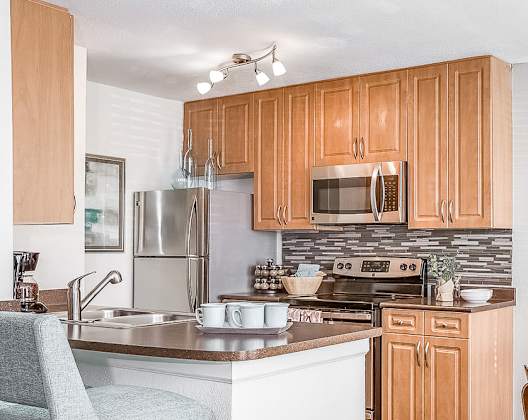 A kitchen with wooden cabinets and a white island with a chair. at Central on the Green Apartment Homes, North Carolina, 27604