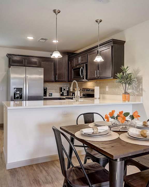 A kitchen with a table set for two with a clock on the wall.