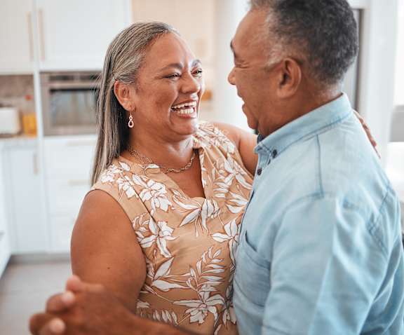 A man and a woman are standing in a kitchen and laughing together.