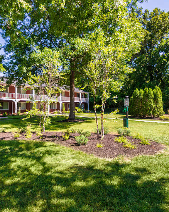 Landscaped courtyard with mature trees, open lawn, and pet station at Colonial Ridge Apartments