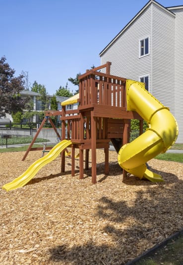 a wooden playset with a yellow slide and a wooden deck with blue chairs in a backyard  at Park Edmonds Apartment Homes, Edmonds, Washington