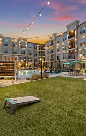 A sunset view of a grassy area with a bench and apartment buildings in the background.