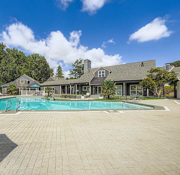 A large outdoor swimming pool surrounded by a paved patio and a building in the background.