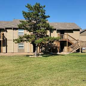 Willow Creek Apartments - Exterior view of the apartment complex surrounded by green lawns and trees.