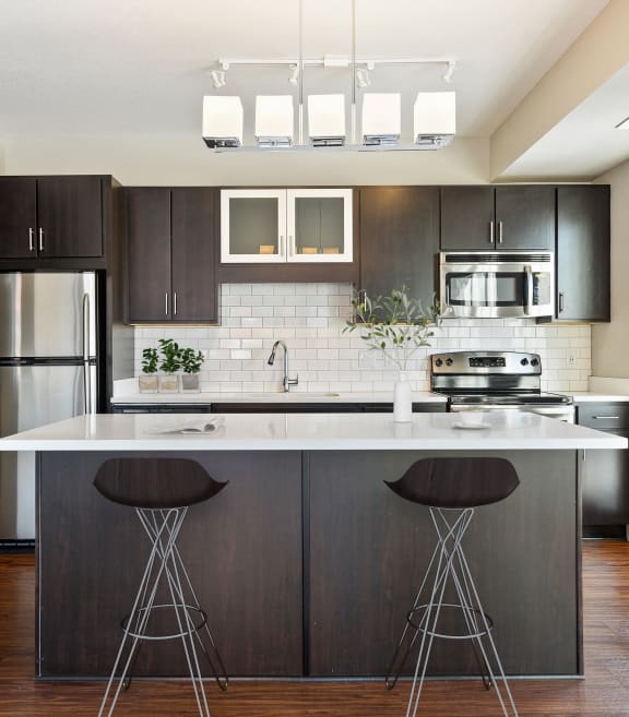 a kitchen with a large island with bar stools and a stainless steel refrigerator