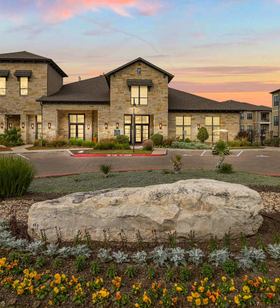 A large rock is in the middle of a flower bed in front of a building. at The Royce at 8100, Austin, TX, 78729