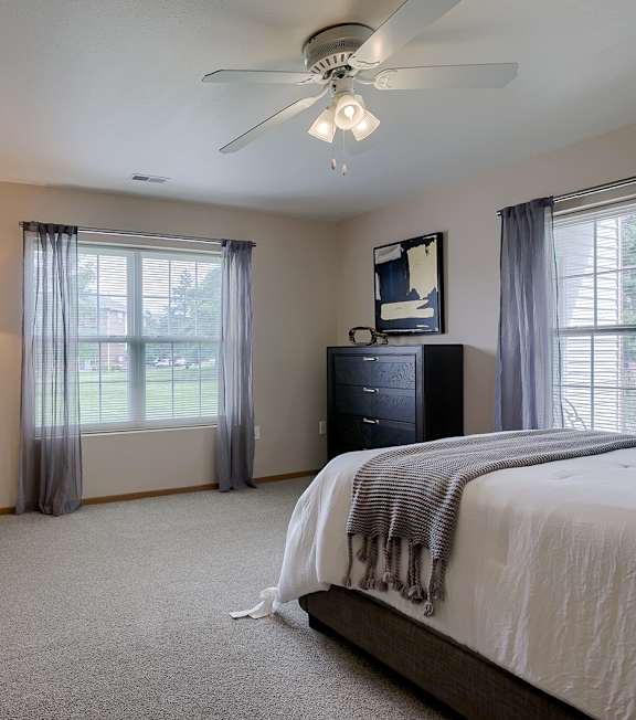 A bedroom with a bed, chair, and a ceiling fan.