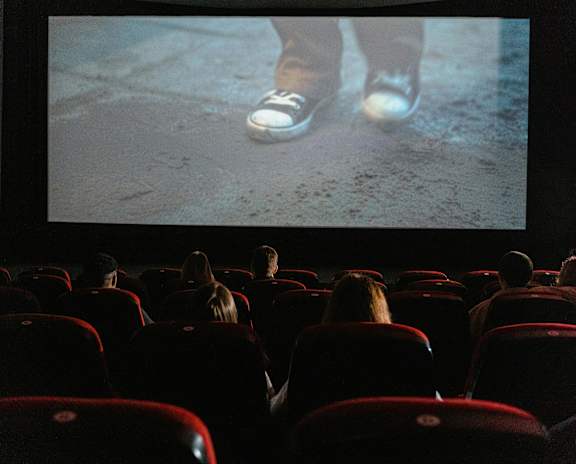 A movie theater with red seats and people watching a film.