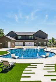 A swimming pool with white lounge chairs and a residential area in the background.