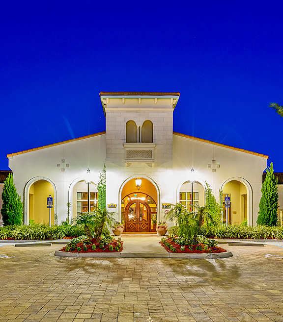 A large house with a lit up entrance and a driveway.