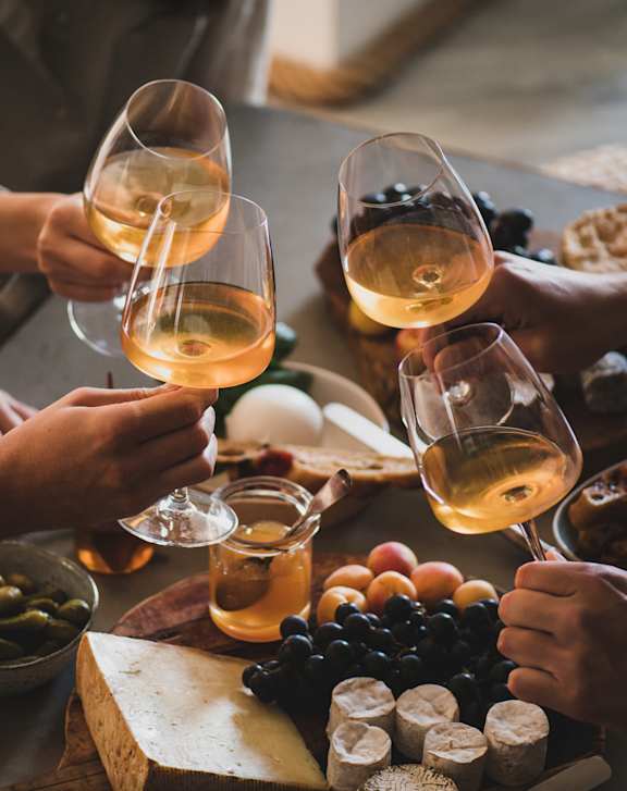 A group of people toasting with wine glasses at a table full of food.